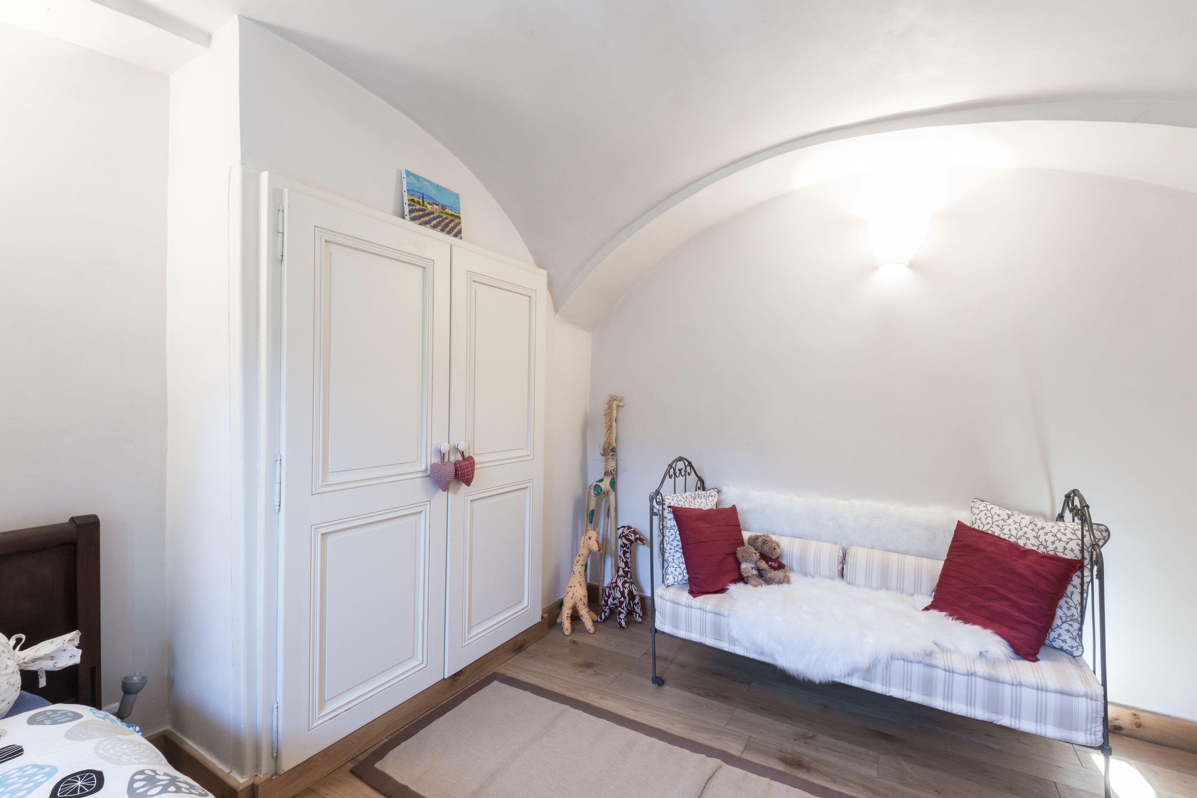 A bedroom with a white sofa, a bed with a wooden headboard, a wardrobe, and a curved ceiling.