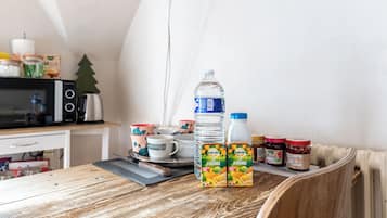 A kitchen with a wooden table, a microwave, a kettle, and various food items including juice boxes and jars.