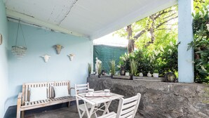 Een overdekt terras met een houten bank en tafel, omgeven door stenen muren en potplanten.