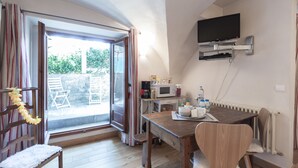Een kamer met een houten eettafel, stoelen, een aan de muur bevestigde televisie en een glazen schuifdeur naar een buitenruimte met stoelen.