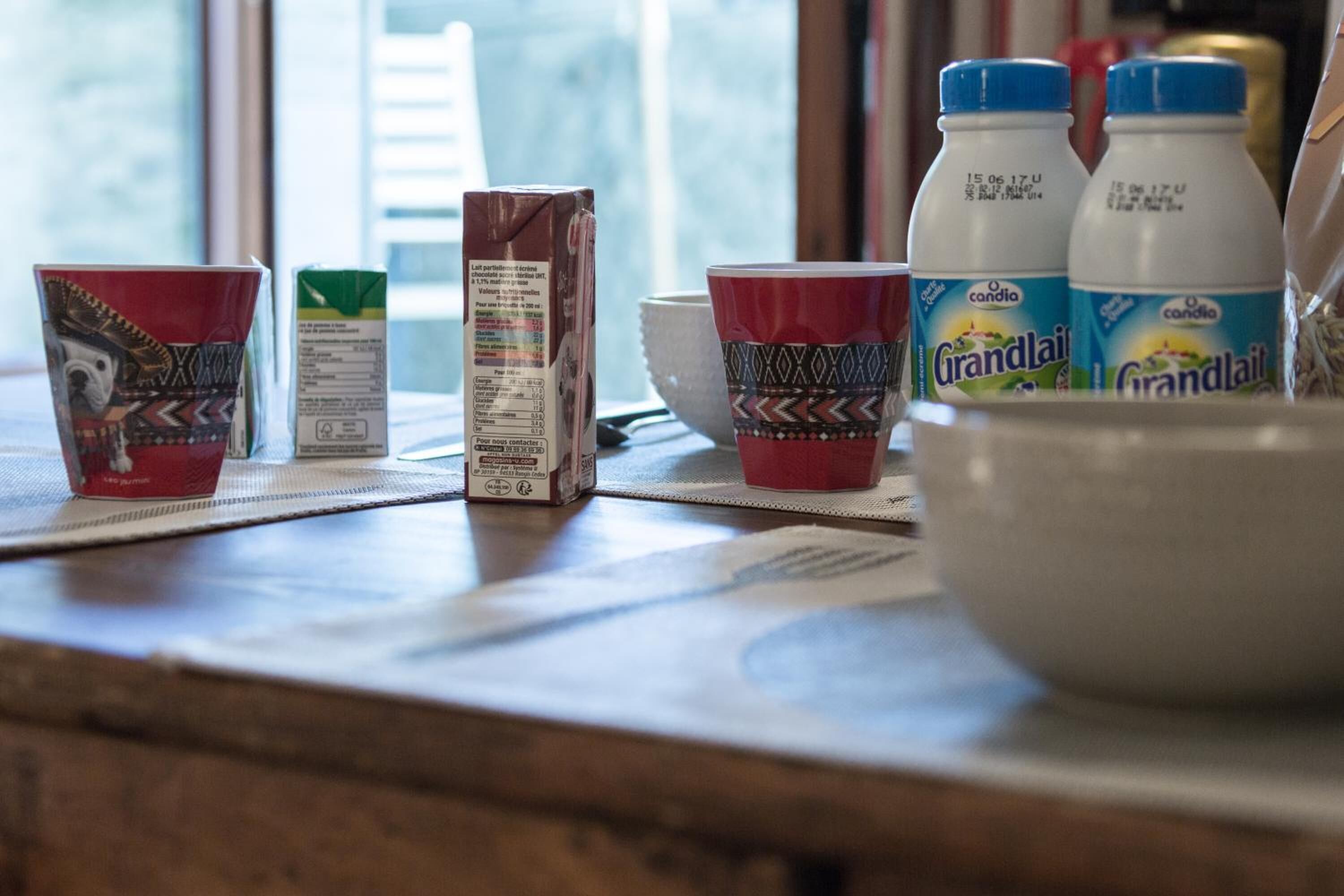 A kitchen counter with a carton of milk, two cups, and two bottles of Grandlait juice.
