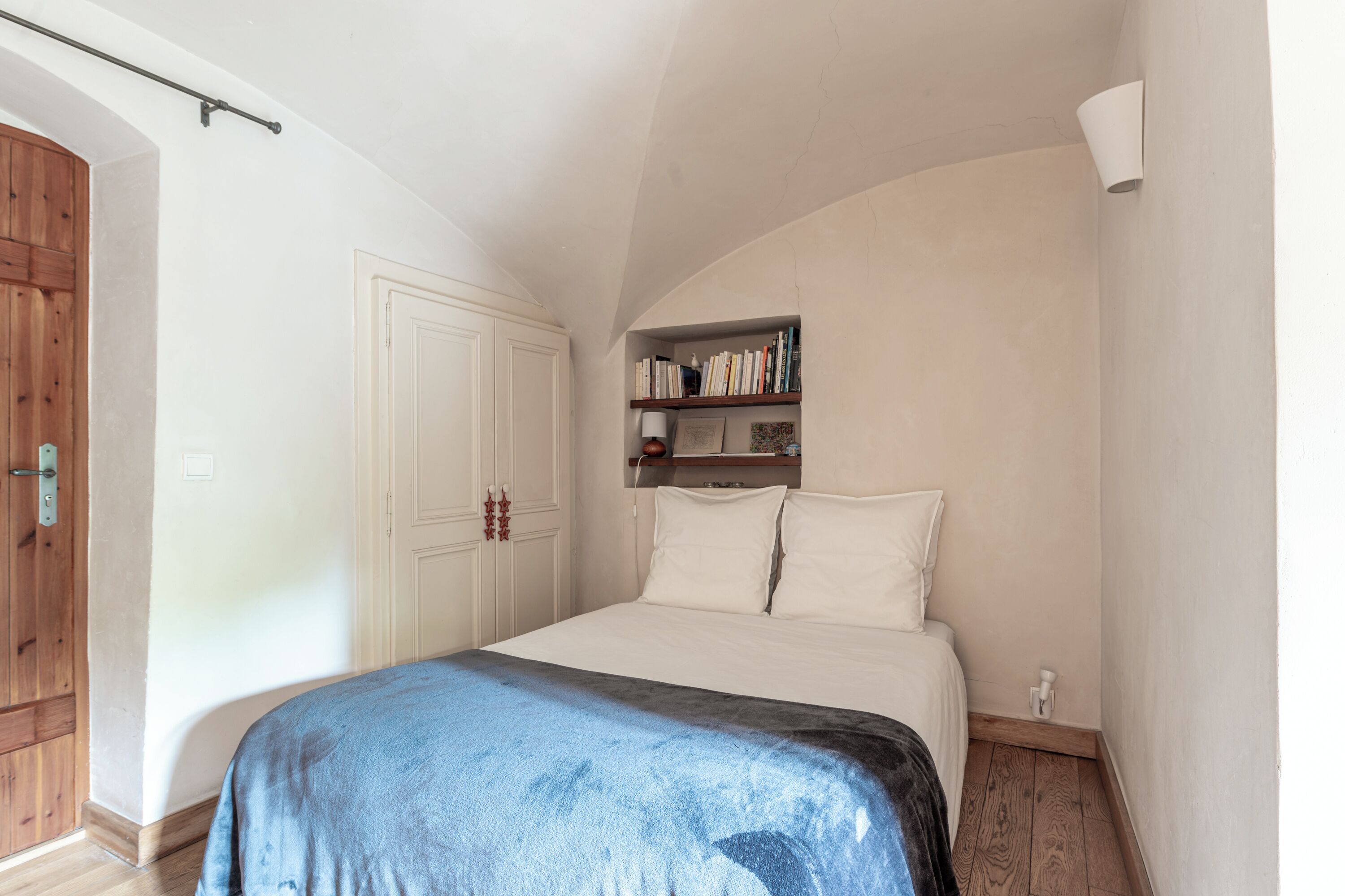 Une chambre à coucher avec un lit, une armoire en bois, une bibliothèque et un mur blanc.