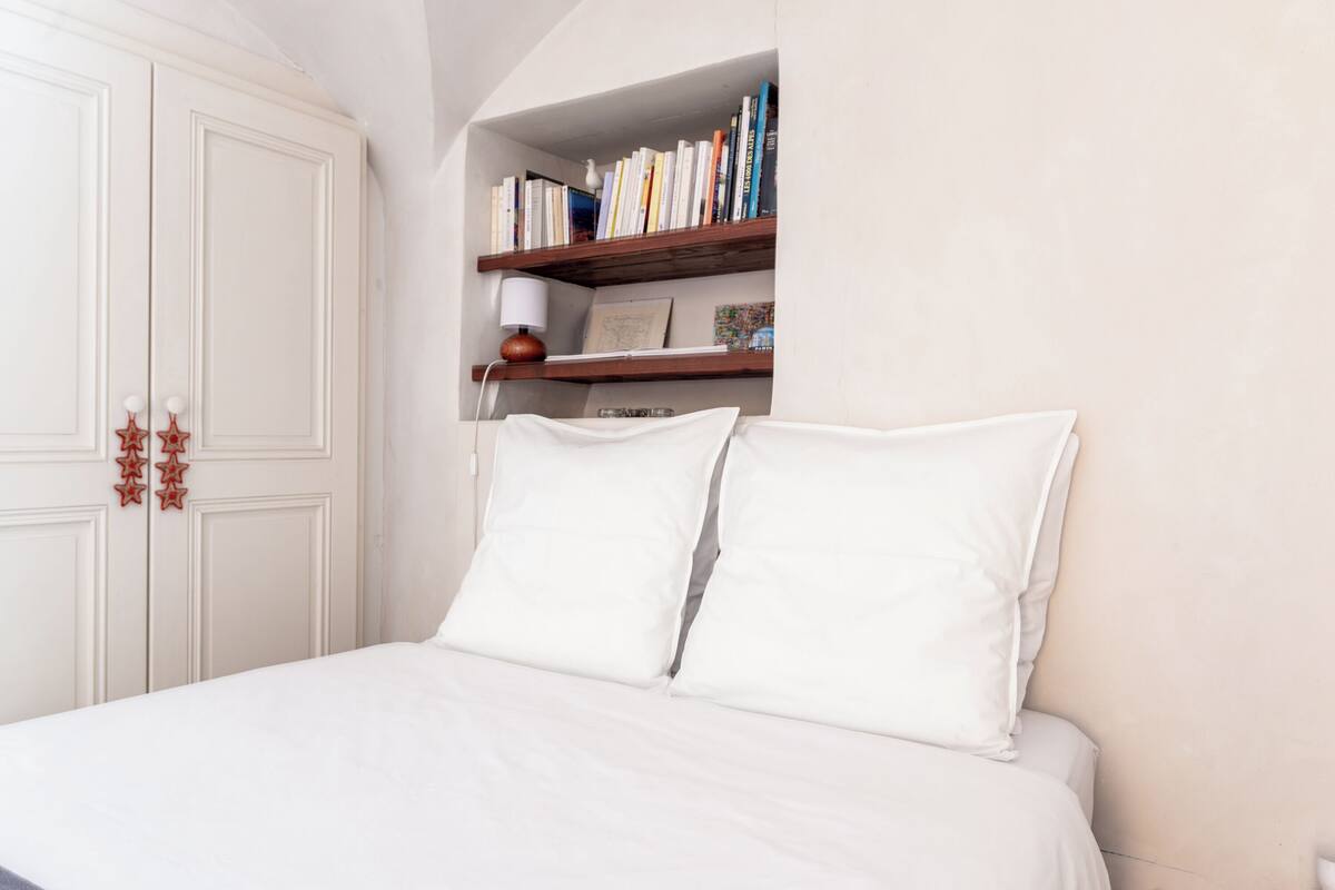 Une chambre avec un grand lit, des murs blancs, une bibliothèque en bois et une armoire.