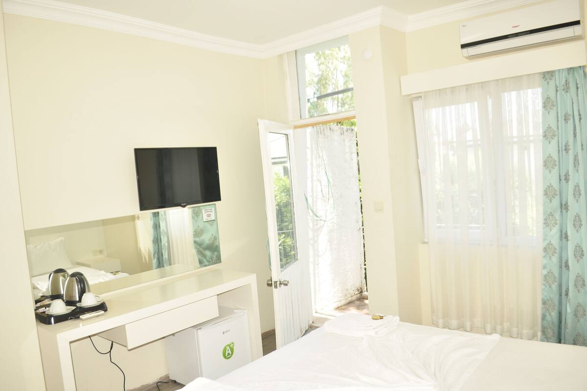 A hotel room with a bed, a desk with a flat-screen TV, a mini-fridge, and a window with curtains.