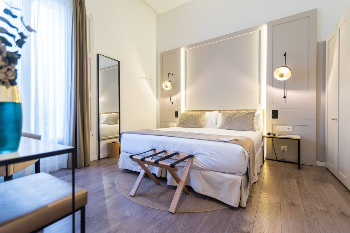 Ein modernes Hotelzimmer mit einem großen Bett, Nachttischen, einem kleinen Schreibtisch und einem Spiegel.
