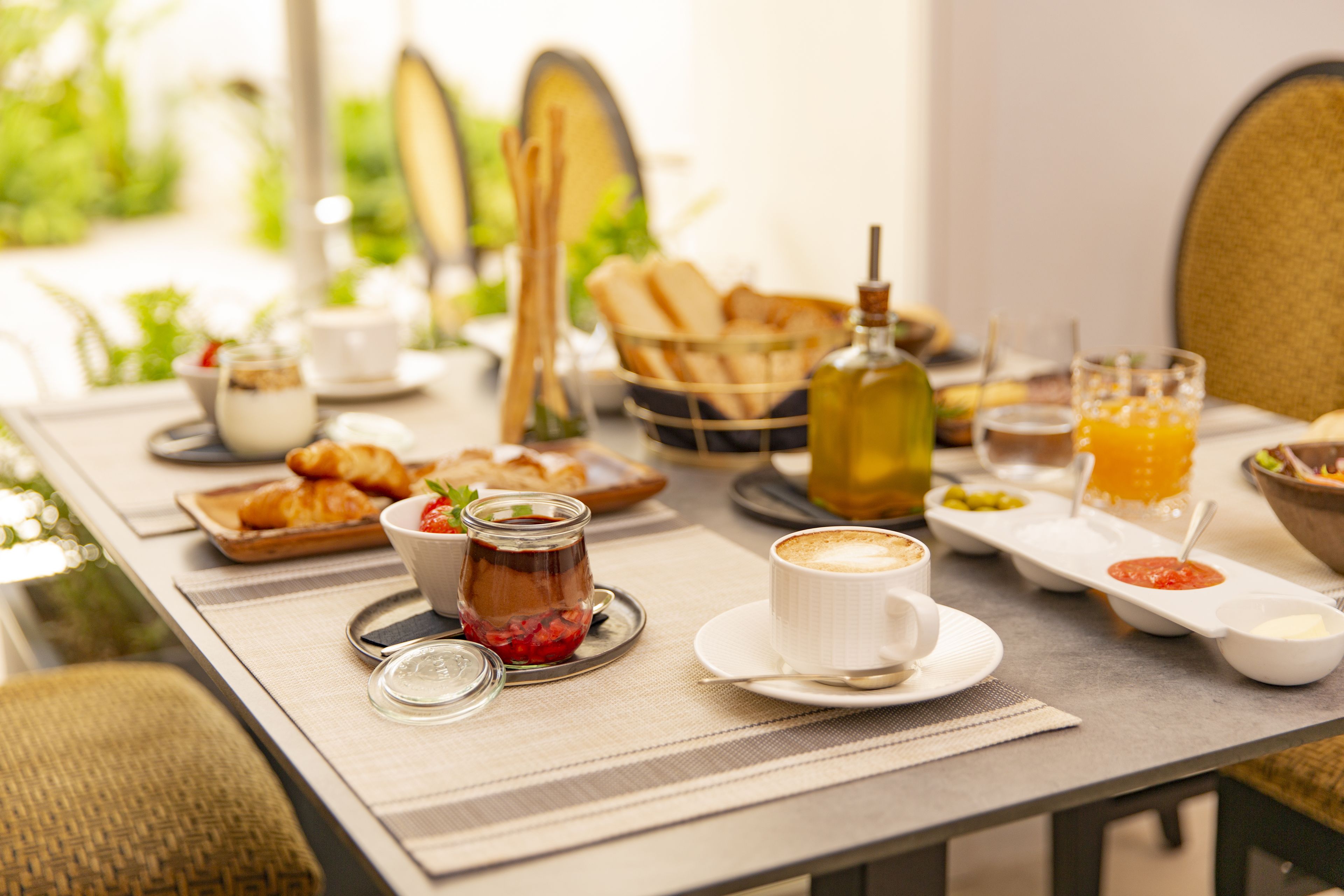 Een ontbijttafel met croissants, een koffiekop, een pot jam en een glas sinaasappelsap.