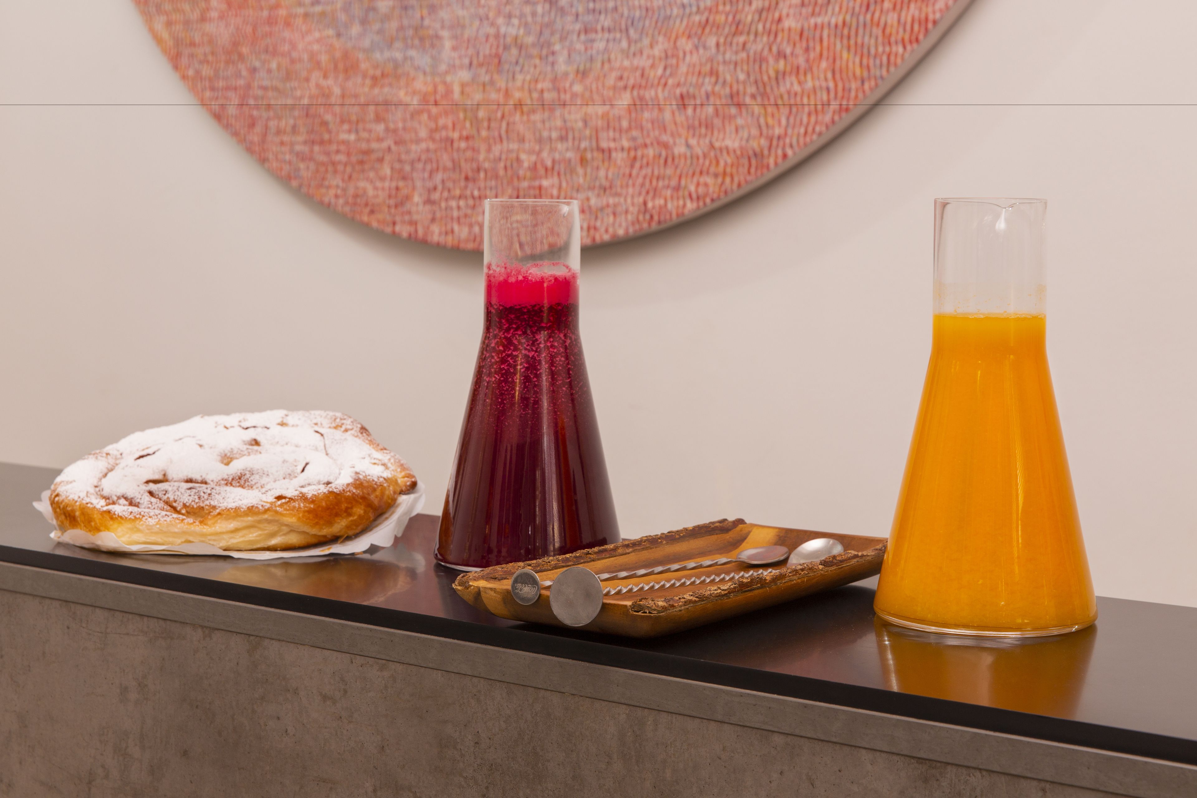 A table with a pastry, a glass of orange juice, and a bottle of red drink.