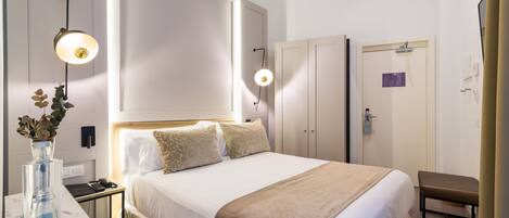 A hotel room with a large bed, bedside tables, a desk, a vase with flowers, and a wall-mounted lamp.