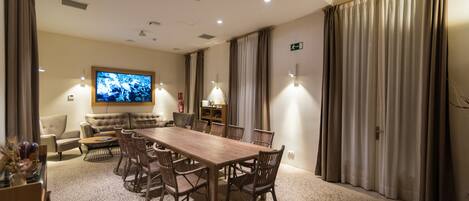 A conference room with a long wooden table, multiple chairs, a sofa, a television, and curtains.