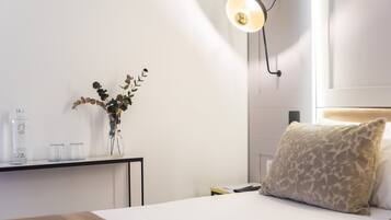 Une chambre d’hôtel bien rangée, avec un lit, une table de chevet ornée d’un vase de fleurs, une lampe et un luminaire fixé au mur.