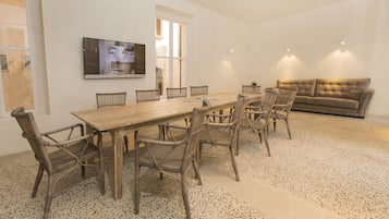A spacious room with a wooden dining table surrounded by wicker chairs, a beige sofa, and a television mounted on the wall.