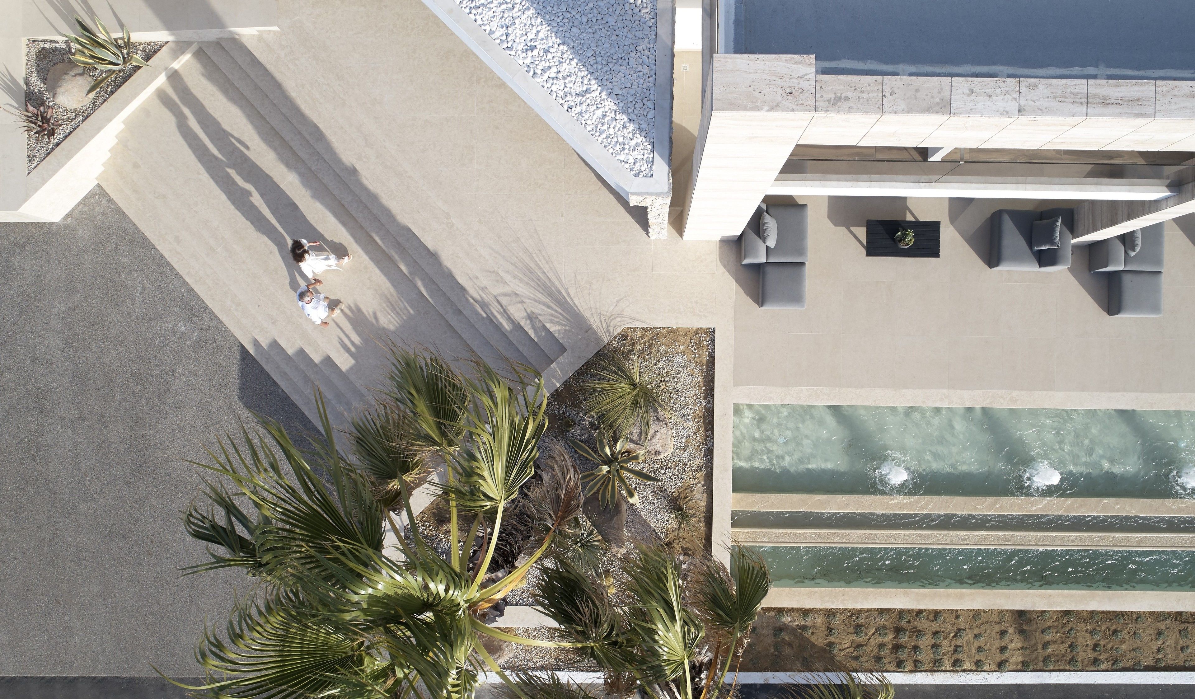 An aerial view of a modern hotel with a pool, outdoor seating, and palm trees.