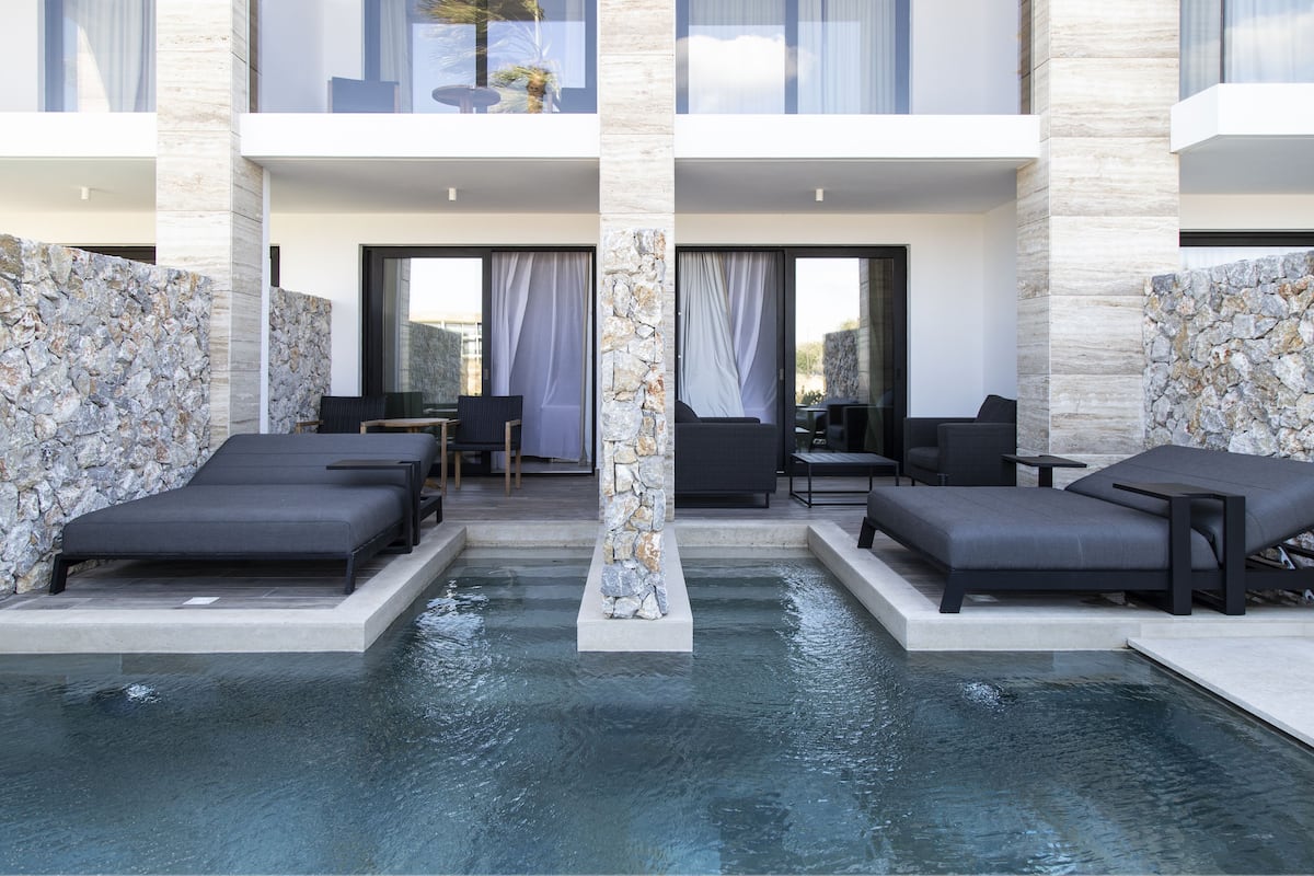 Un espace piscine extérieur moderne, doté de chaises longues et d’un pilier en pierre.