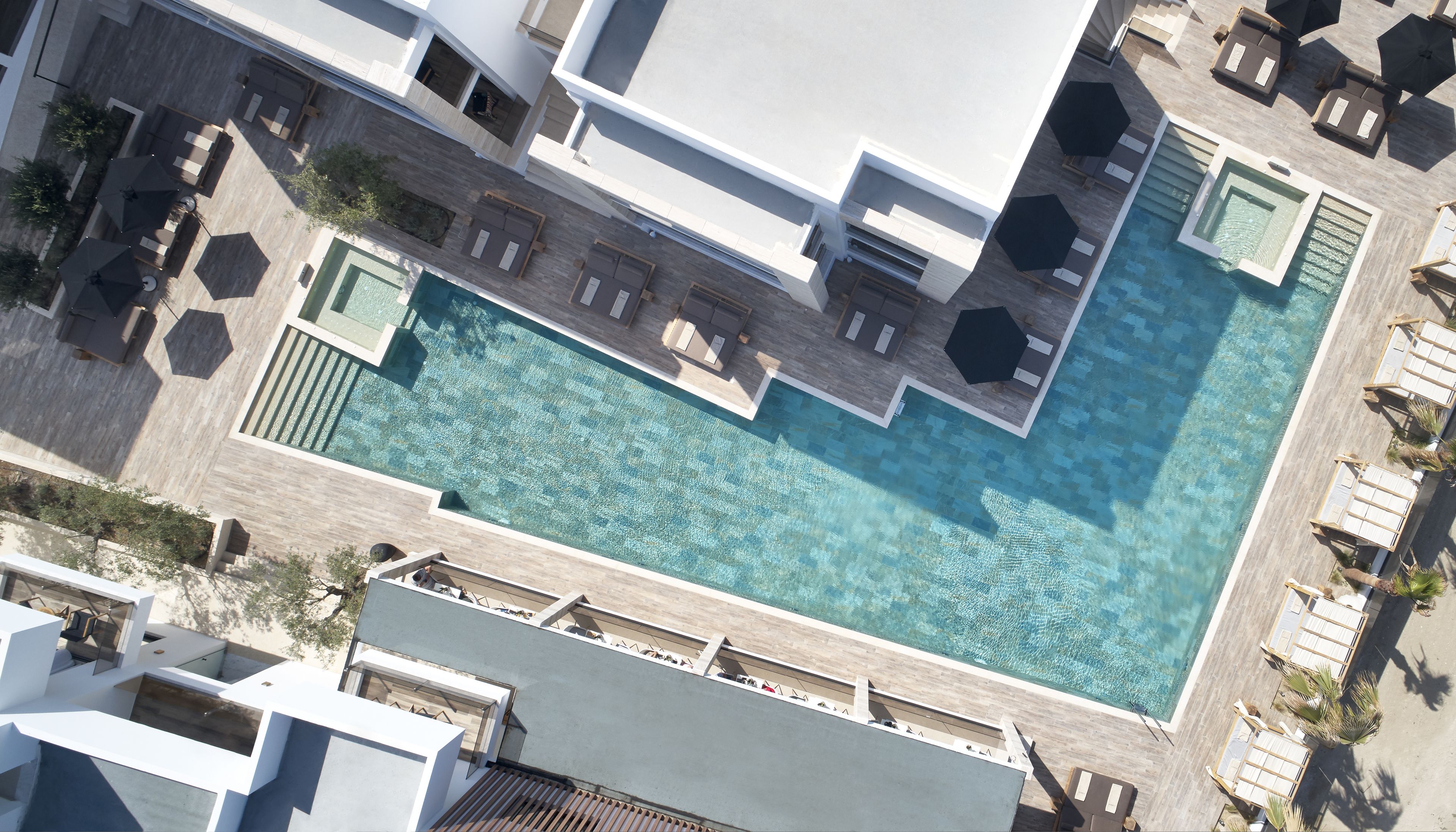 Ein Luftbild eines modernen Hotels mit großem, zentral gelegenen Schwimmbad, Liegestühlen und einer Dachterrasse.
