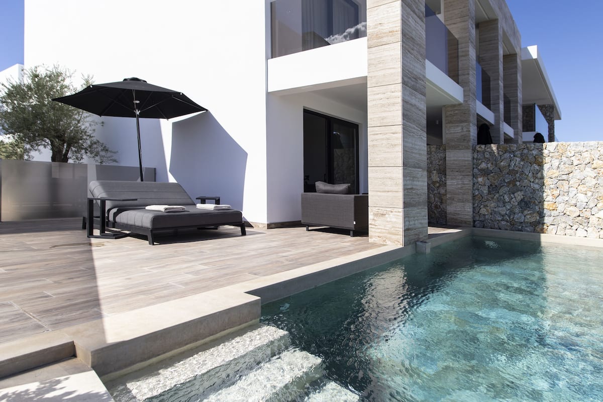 Un espace piscine extérieur moderne, doté d’une chaise longue et d’un parasol, d’un mur en pierre et offrant une vue dégagée sur la piscine.