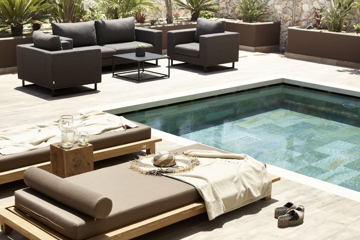 Un espace aménagé au bord de la piscine, avec des chaises longues, une petite table où sont posées des boissons, et un mur de pierre en arrière-plan.