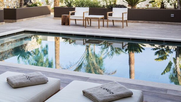 Un área junto a la piscina con dos sillones de descanso, una mesita y un banco.