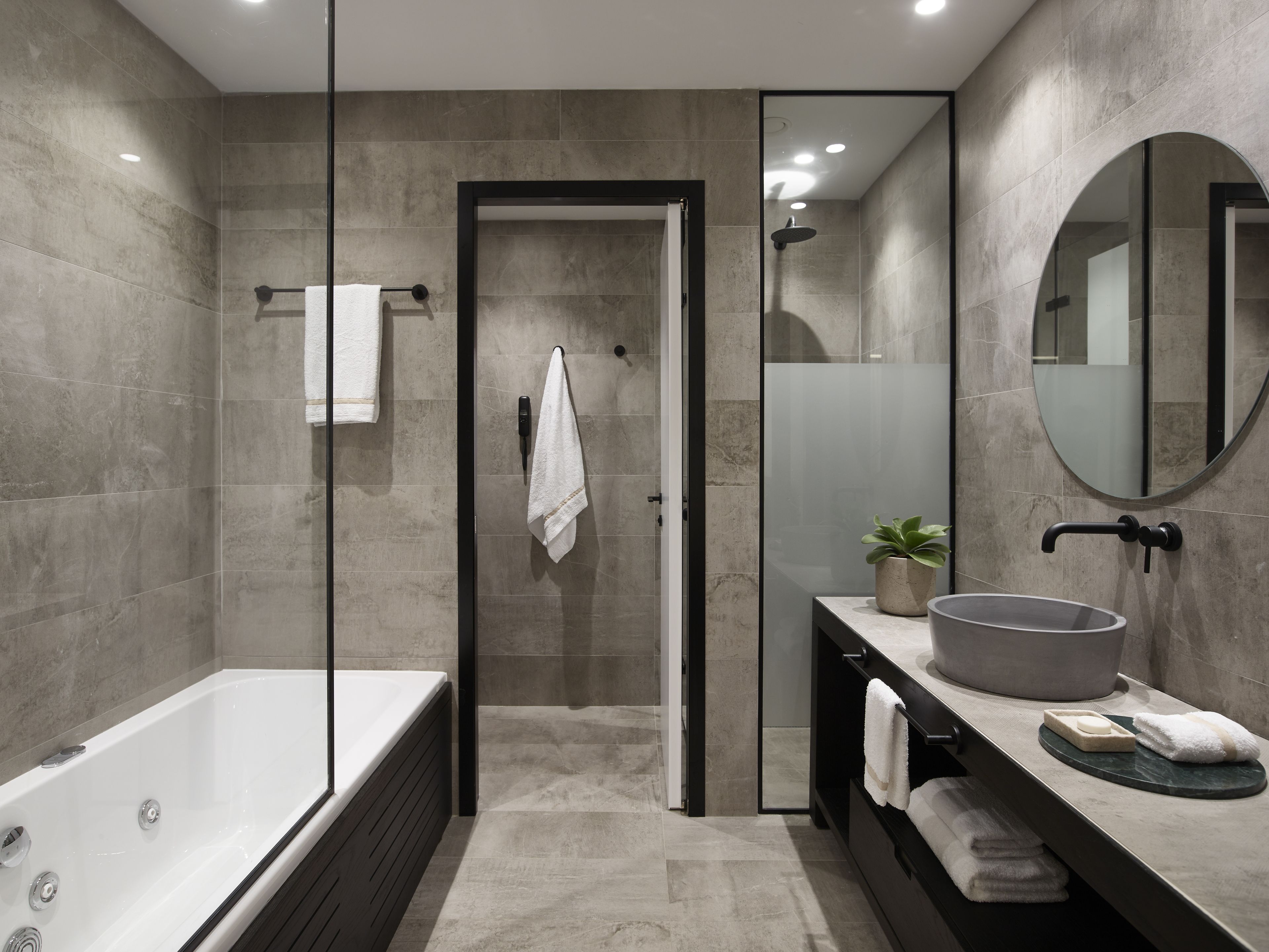 A modern bathroom with a glass-enclosed shower, a large bathtub, and a vanity with a round sink.