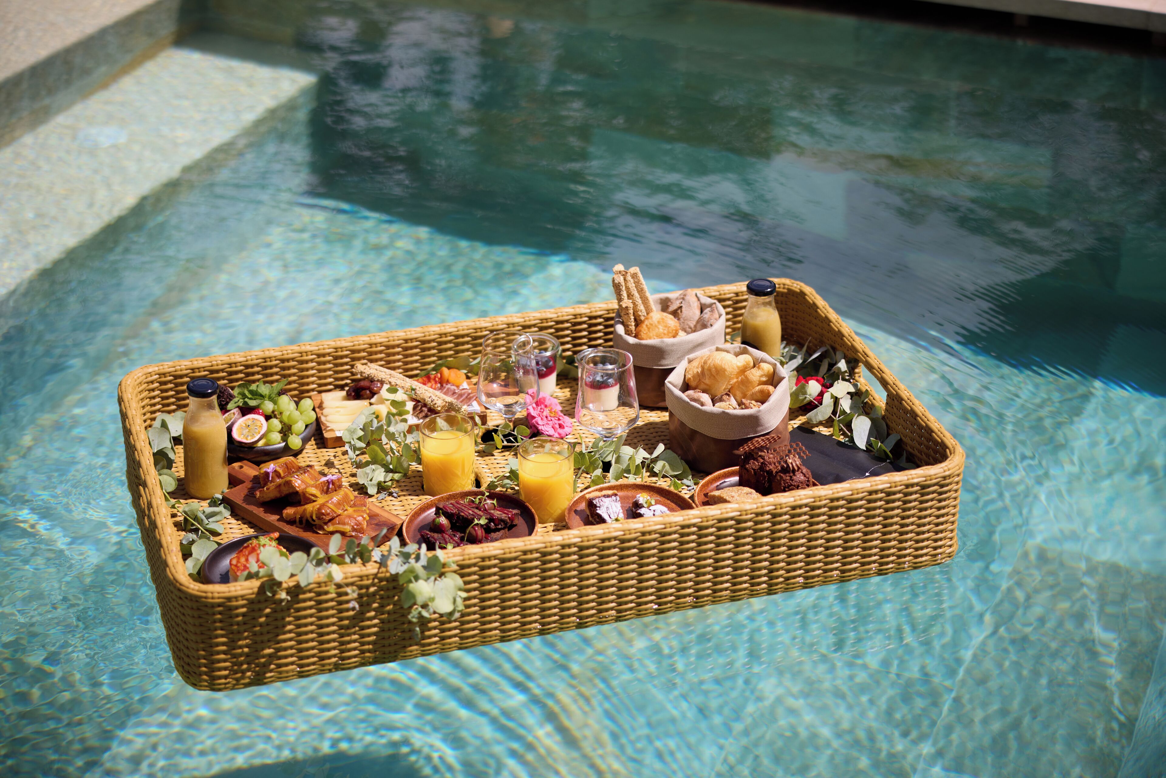 A floating tray with food and drinks over a pool.