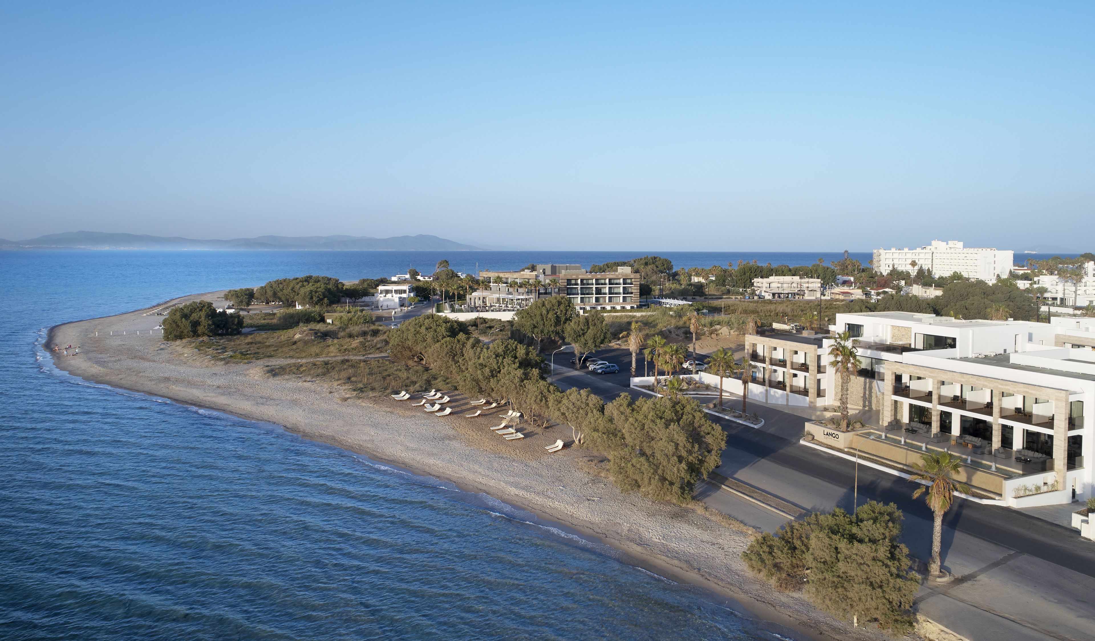 A coastal hotel with a beach view, multiple buildings, and parked cars.