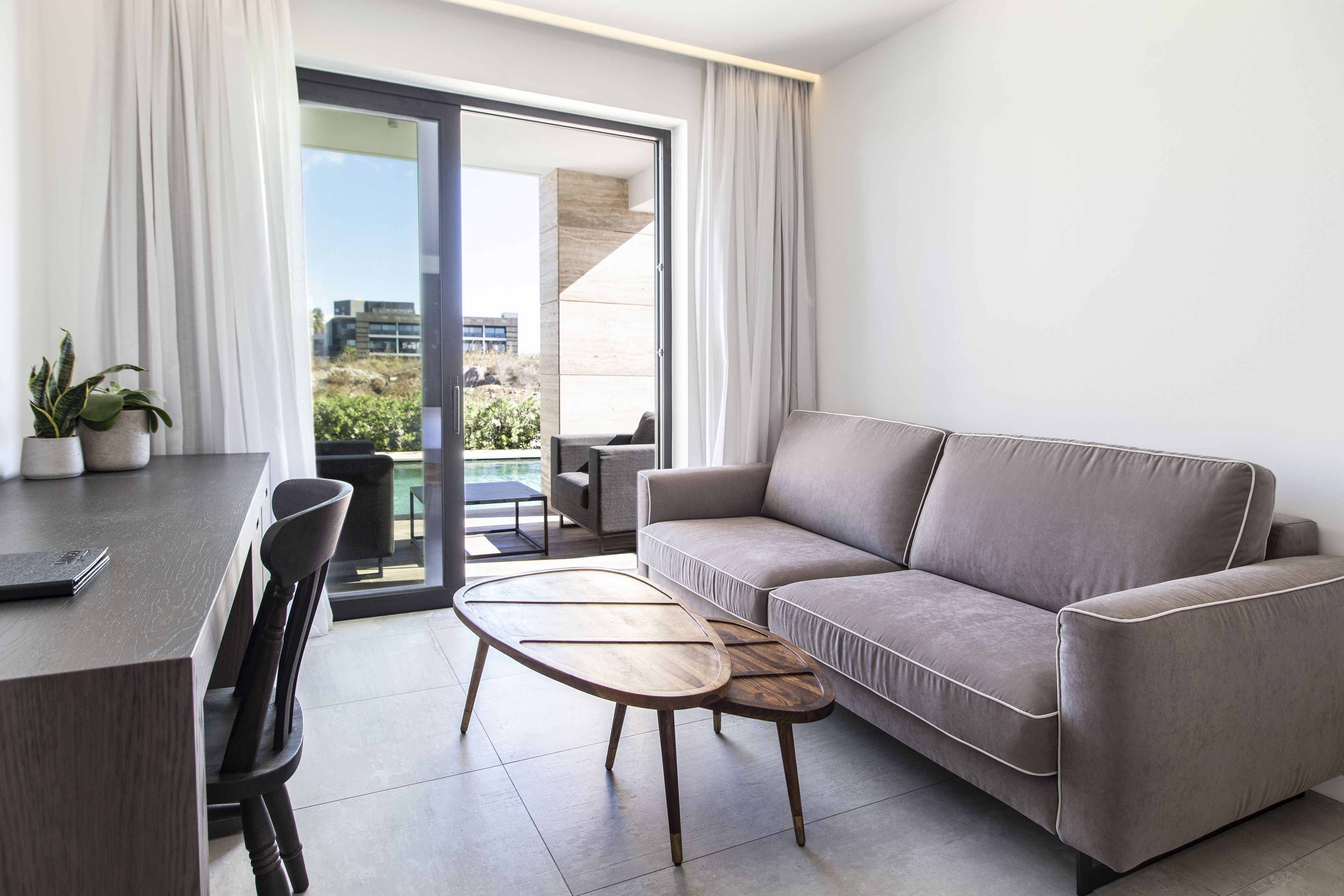 A modern living room with a sofa, a dining table, and chairs. There is a sliding glass door leading to an outdoor area.
