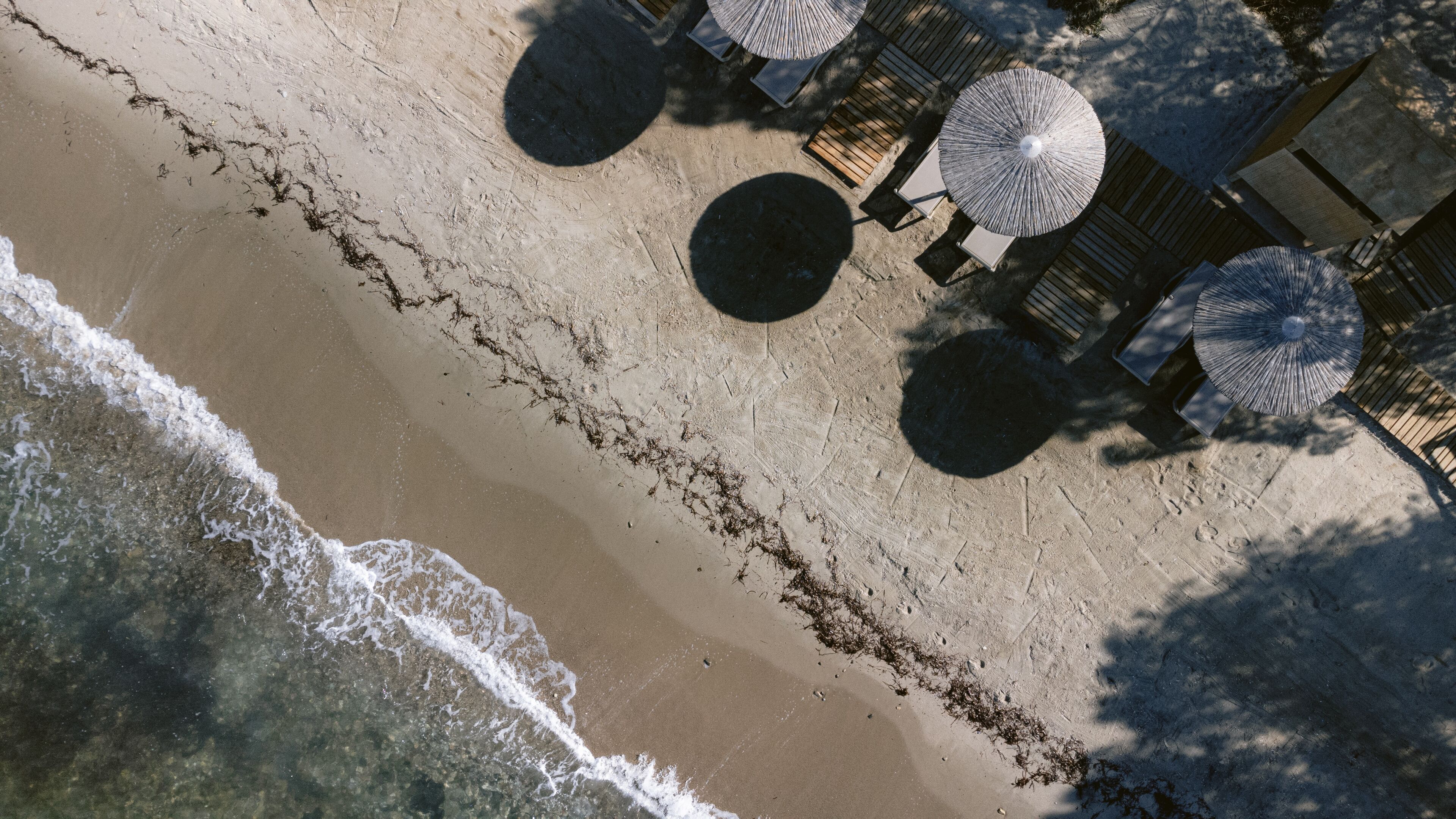 An aerial view of a beach with a wooden deck, umbrellas, and lounge chairs.