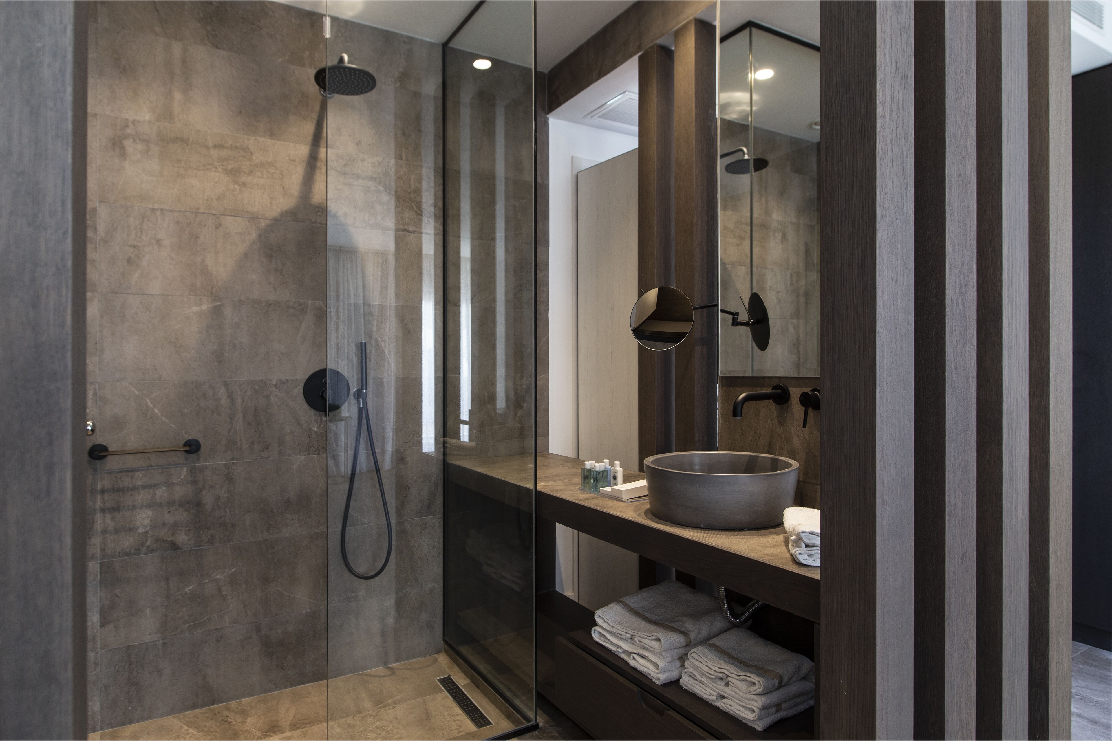 Un bagno moderno con doccia vetrata, uno specchio grande e un mobile bagno in legno con lavabo.
