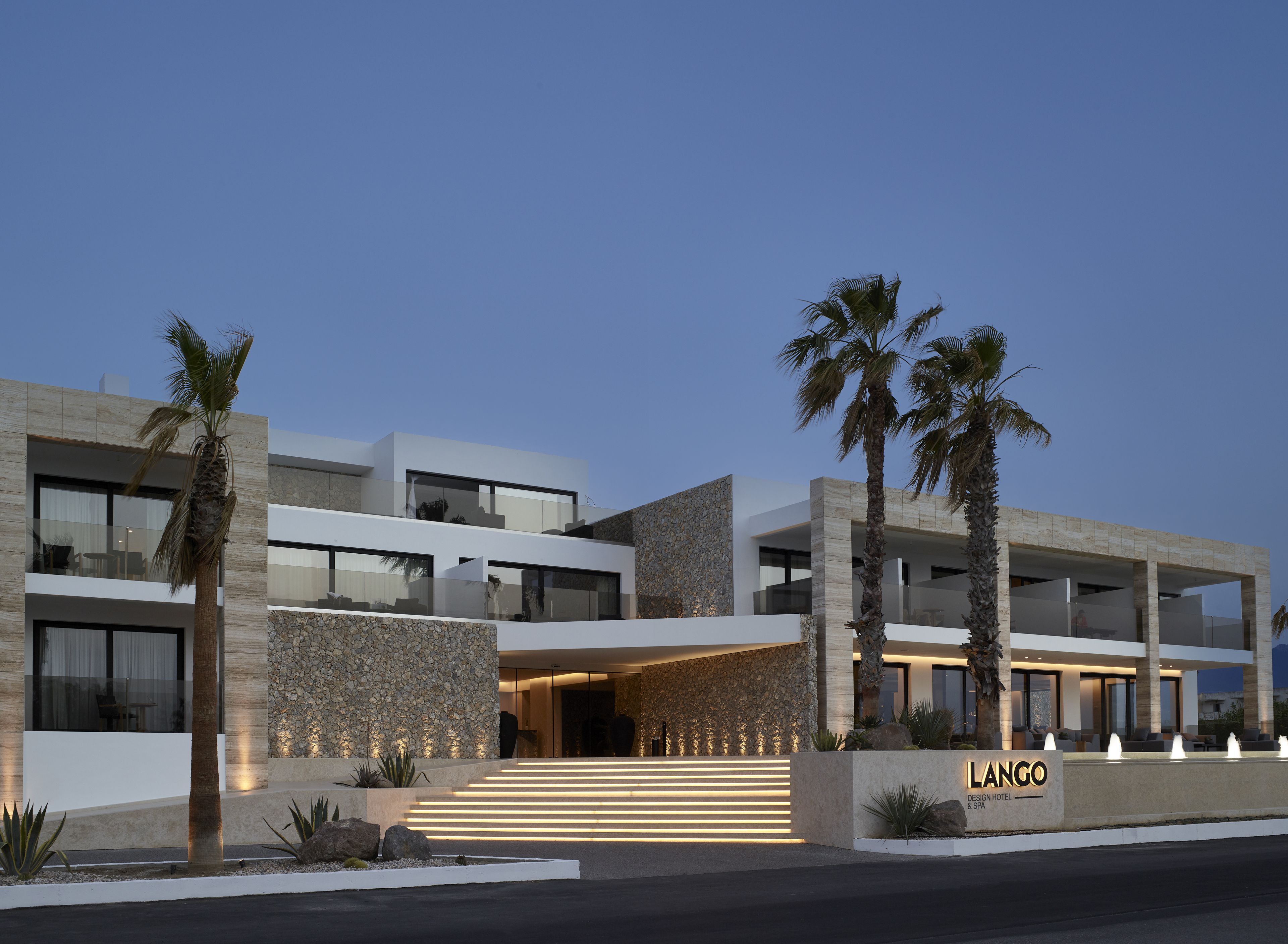 A modern hotel with a stone facade, multiple balconies, and palm trees.