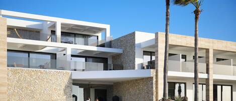 A modern hotel with a stone facade, multiple balconies, and palm trees.