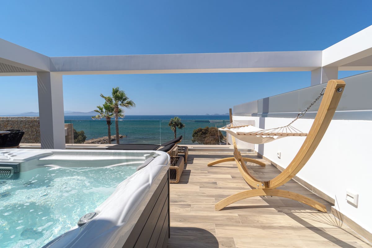 Une terrasse sur le toit avec un jacuzzi, des fauteuils suspendus en bois et une vue sur la mer.