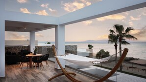 Un espacio exterior moderno con una hamaca, una mesa de comedor con sillas y vista al mar.