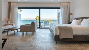 Habitación de hotel moderna con una cama grande, un sofá, una mesa de centro y vistas al mar.