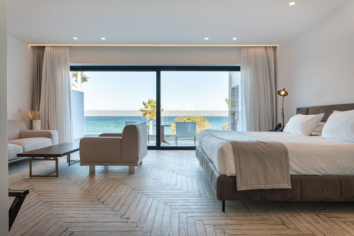 Une chambre d’hôtel moderne avec un grand lit, un canapé, une table basse et une vue sur la mer.
