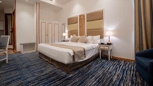 A hotel room with a large bed, bedside tables, a chair, and a view of the hallway. - Platinum Alkhamseen Serviced Apartments (Taif)