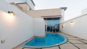 A swimming pool with a tiled deck, a covered seating area, and a view of the interior through a glass door. - Platinum Alkhamseen Serviced Apartments (Taif)