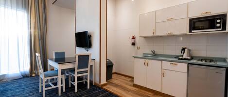 Una habitación de hotel compacta con zona de comedor, pequeña cocina y televisor de pantalla plana.