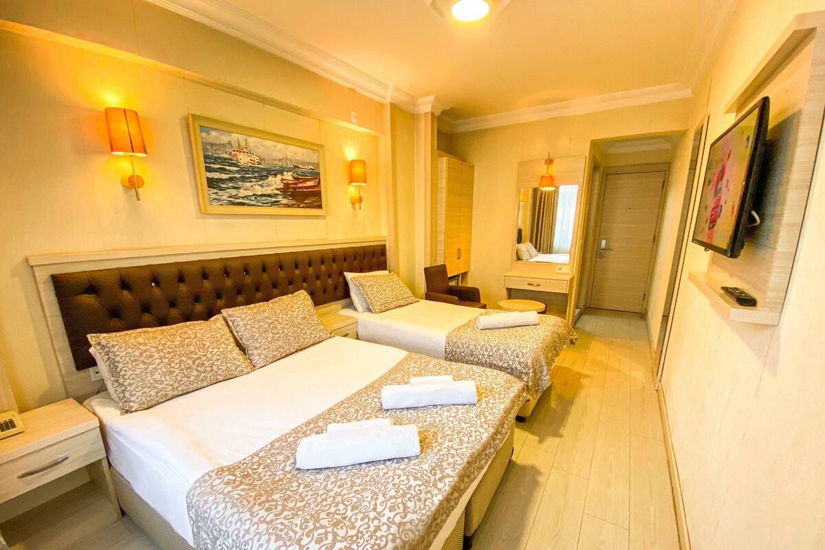 A hotel room with two beds, a large window, a painting, and a TV on the wall.