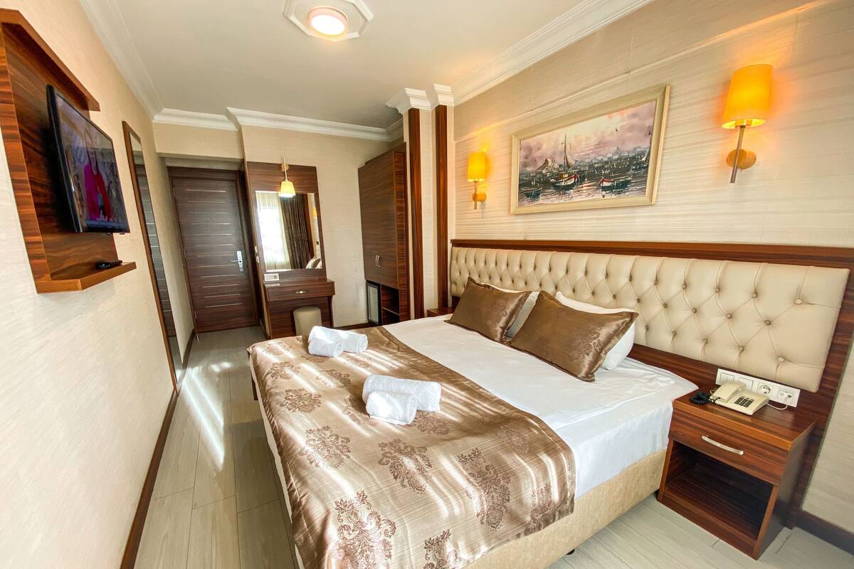 A hotel room with a large bed, a bedside telephone, a wooden nightstand, a mirror, and a painting on the wall.