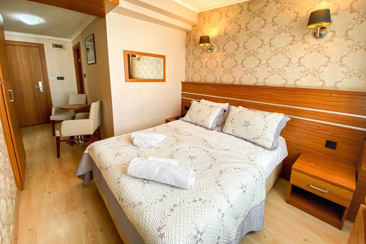 A hotel room with a bed, bedside tables, a chair, and a small table.