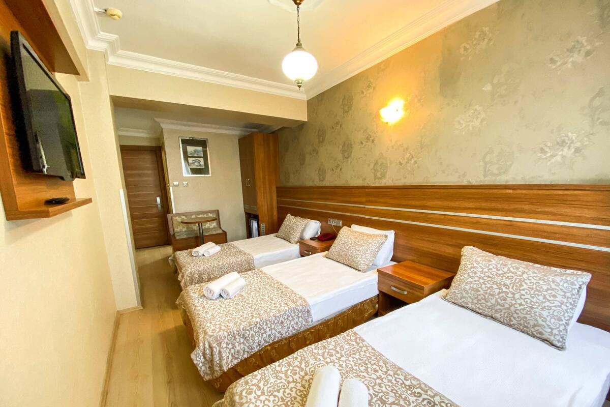A hotel room with two beds, a wooden headboard, a bedside table, a TV mounted on the wall, and a wall-mounted light fixture.