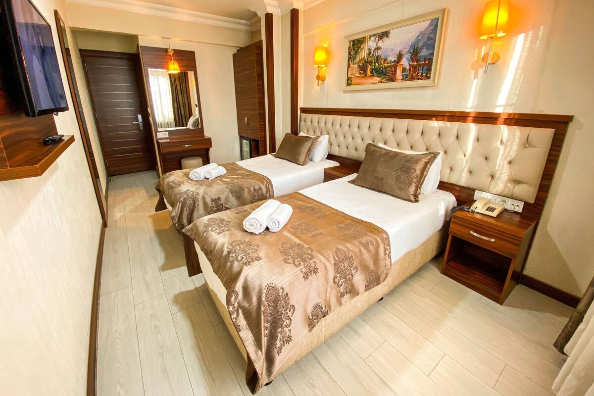 A hotel room with two beds, a wooden headboard, a painting on the wall, and a bedside table with a phone.