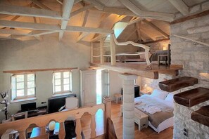 A loft bedroom with a sloped ceiling, wooden beams, stone walls, and a loft bed.