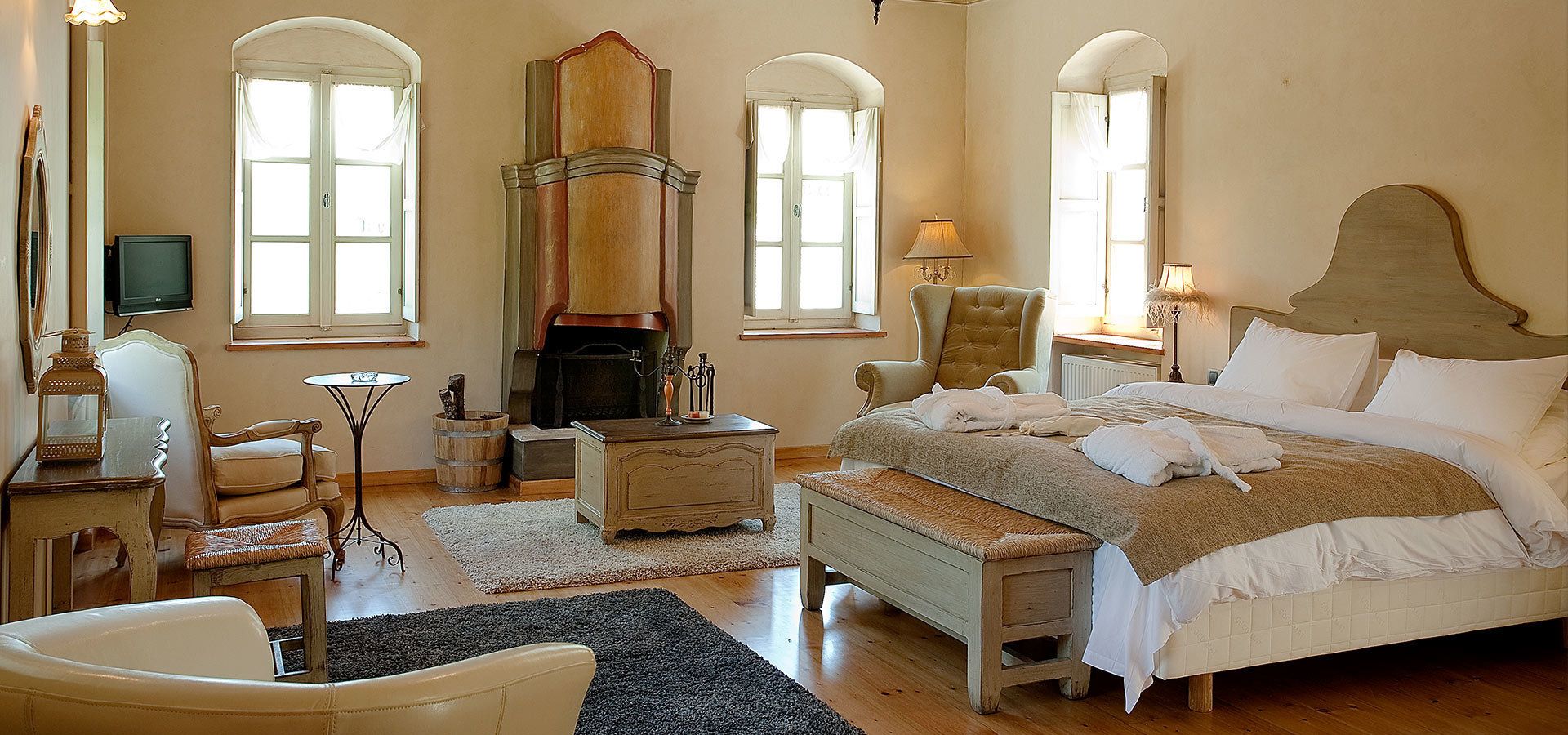 A bedroom with a large bed, a fireplace, a chair, a table, and a television.