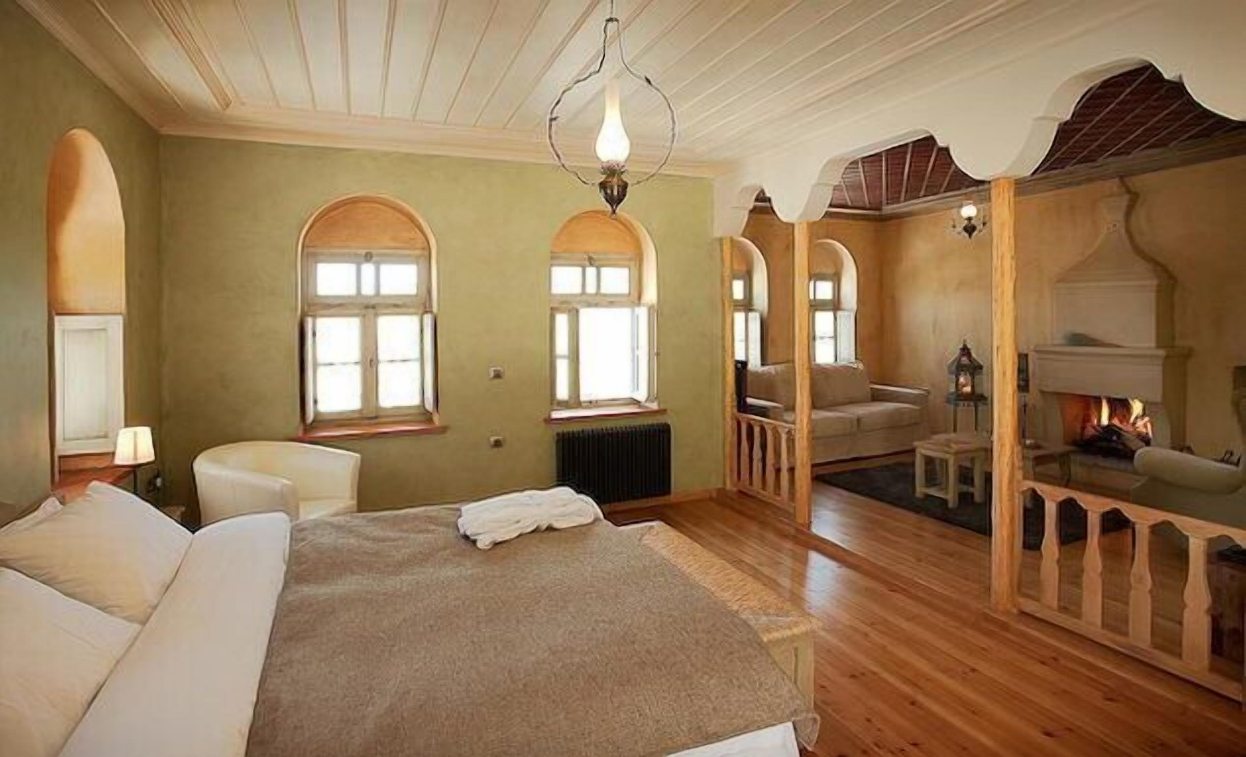 A spacious bedroom with a large bed, two windows, a fireplace, and a cozy seating area.