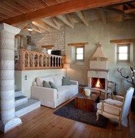 A cozy living room with a stone fireplace, wooden beams, and a white sofa.