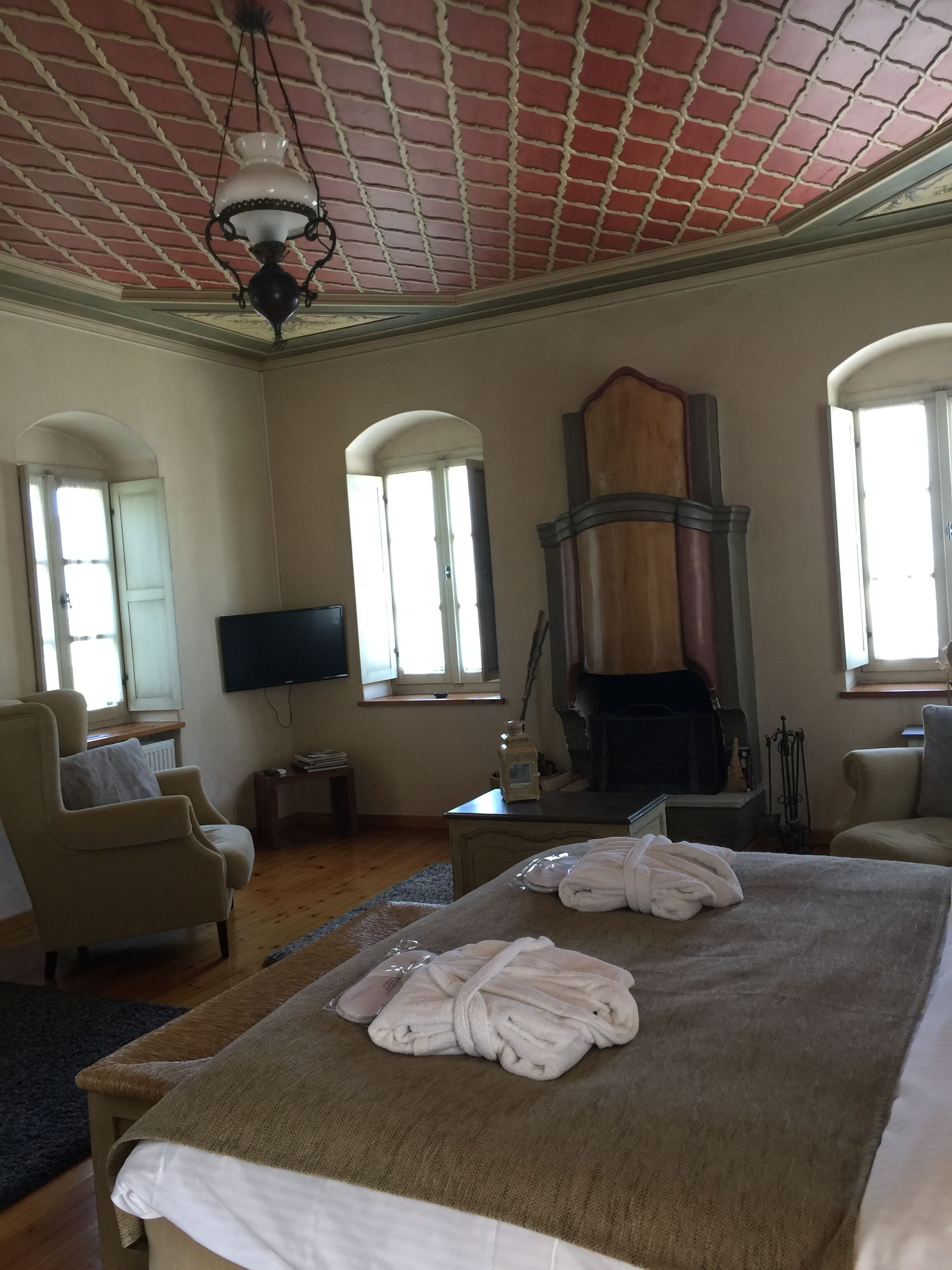 A spacious bedroom with a large bed, two armchairs, a television, and a fireplace.