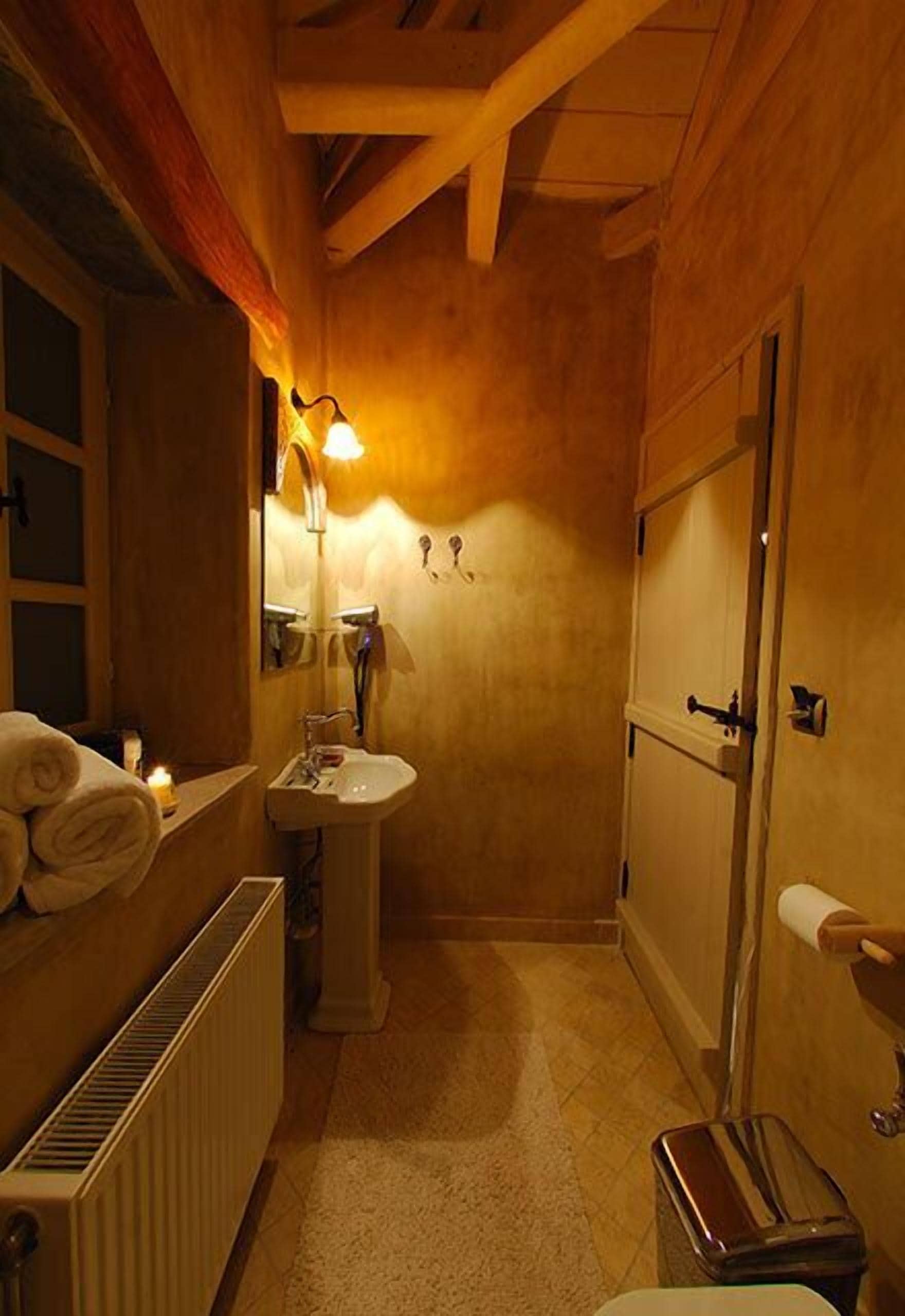 Un baño estrecho con paredes de madera, un lavamanos blanco, un espejo, un perchero para toallas y un radiador.