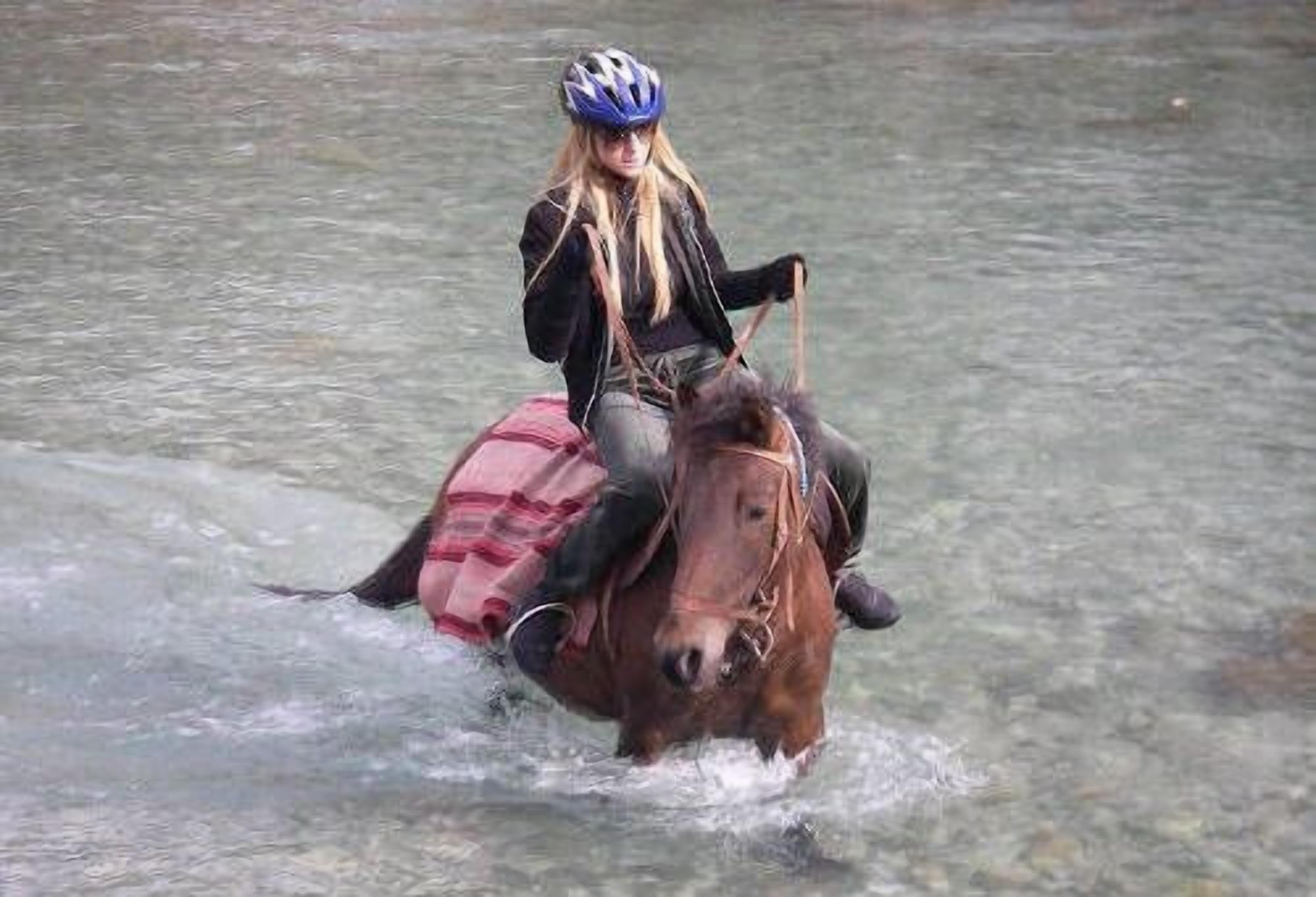 Une personne à cheval traversant une étendue d’eau peu profonde.