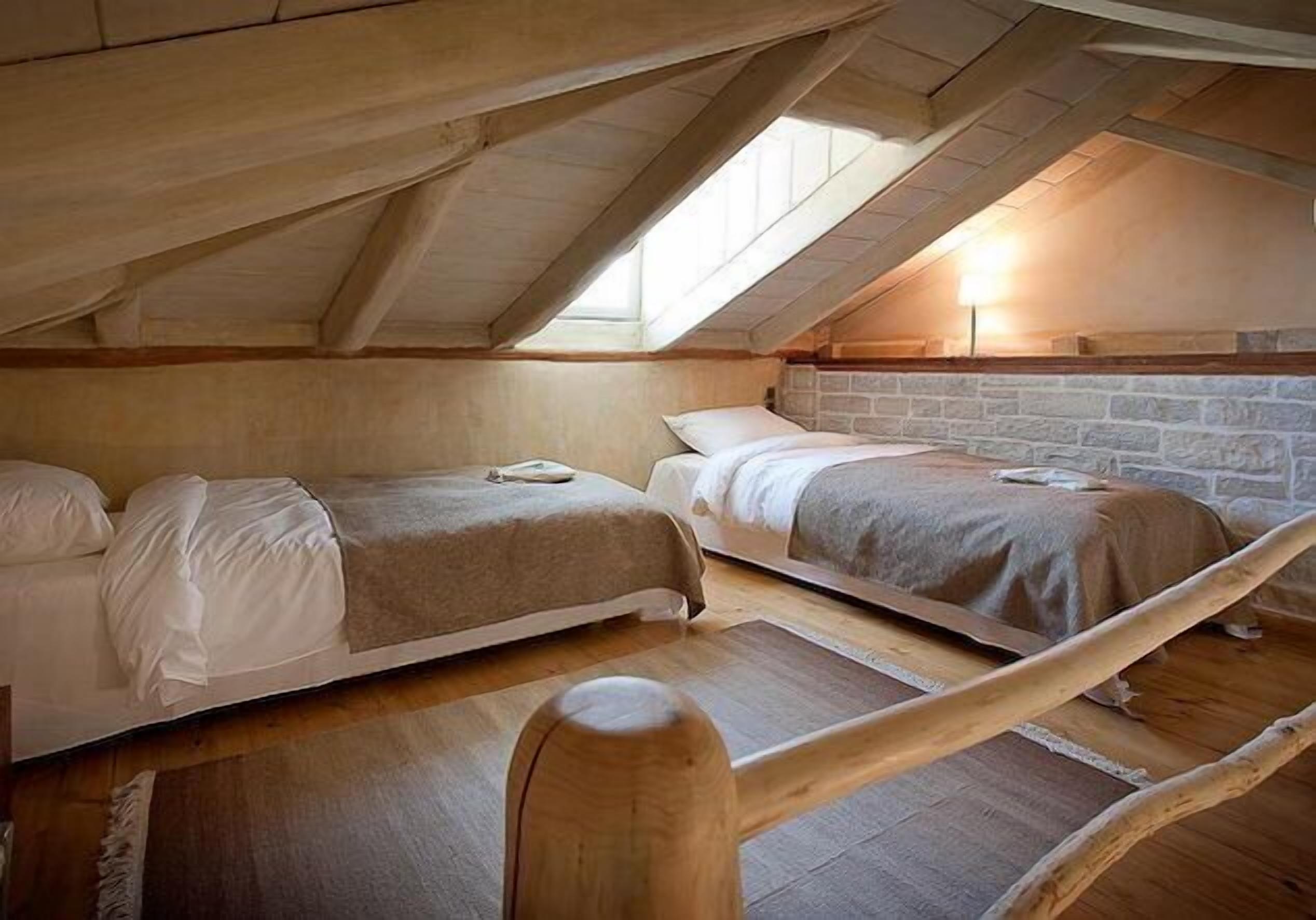 Dormitorio tipo loft con dos camas, vigas de madera y pared de piedra.
