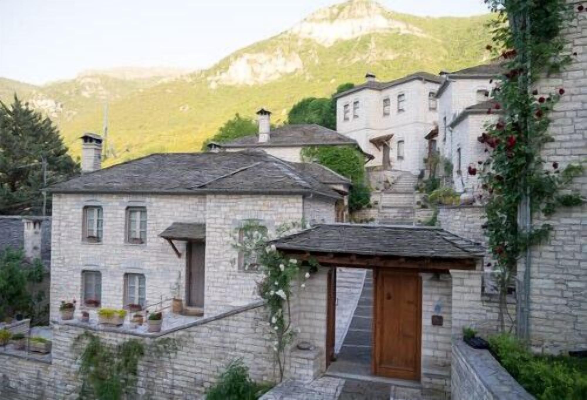 A stone building with a wooden door, surrounded by greenery and a mountain in the background.